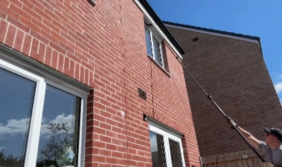 Technician using a water-fed pole to clean an upper-floor window on a brick house