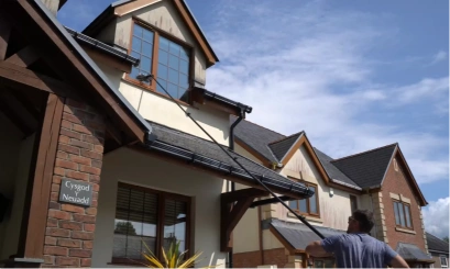 Technician using a long-reach pole to clean upper-storey windows on a large home
