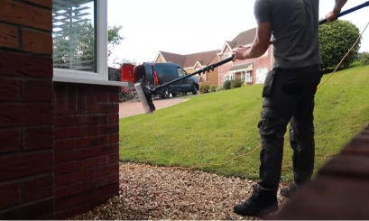 Technician using a pure water-fed pole to clean a bay window on a residential street