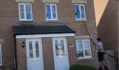 Technician using a water-fed pole to clean upper-floor windows of a two-storey house